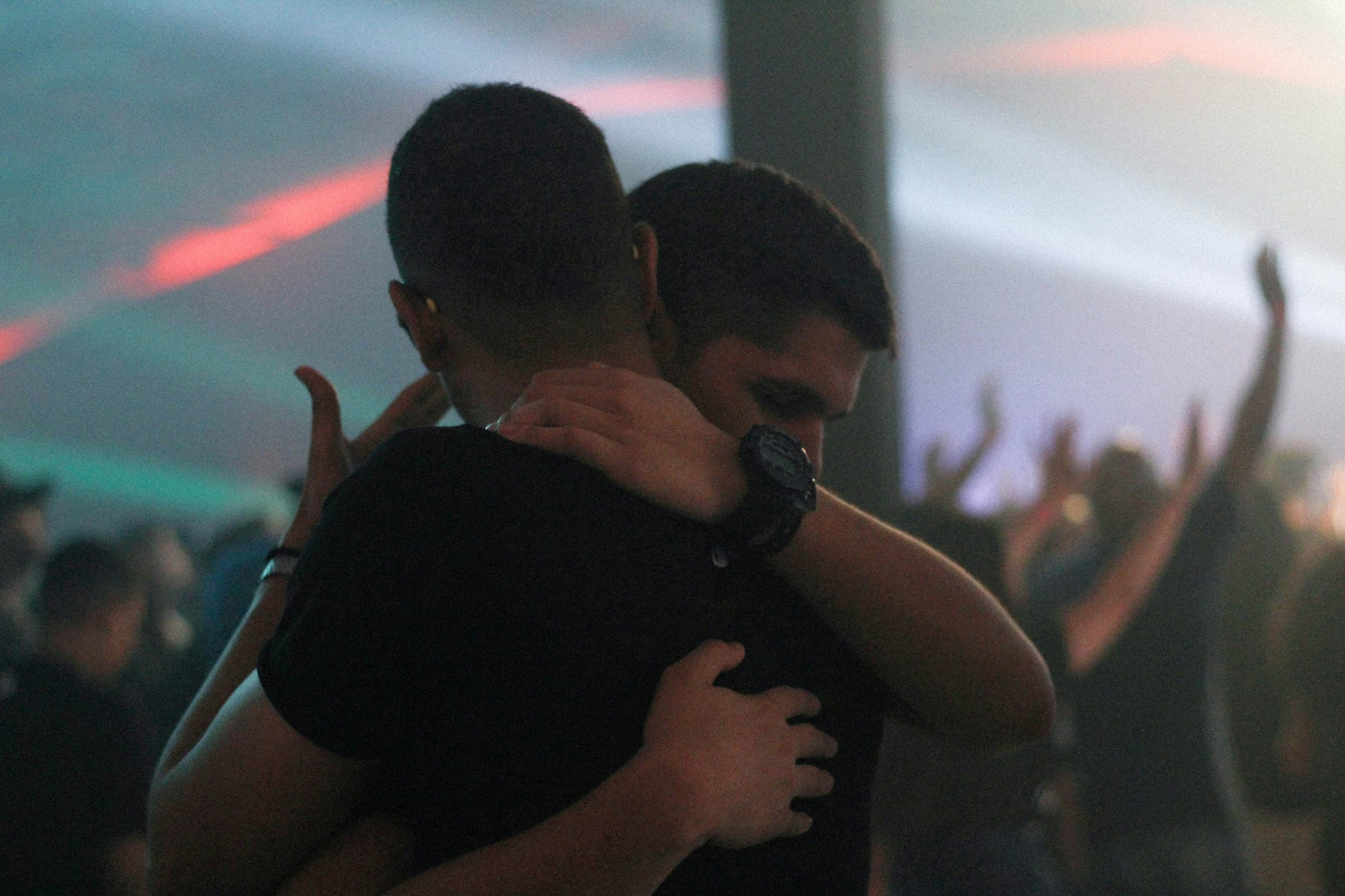 Two men hugging inside a bar with lights behind them.