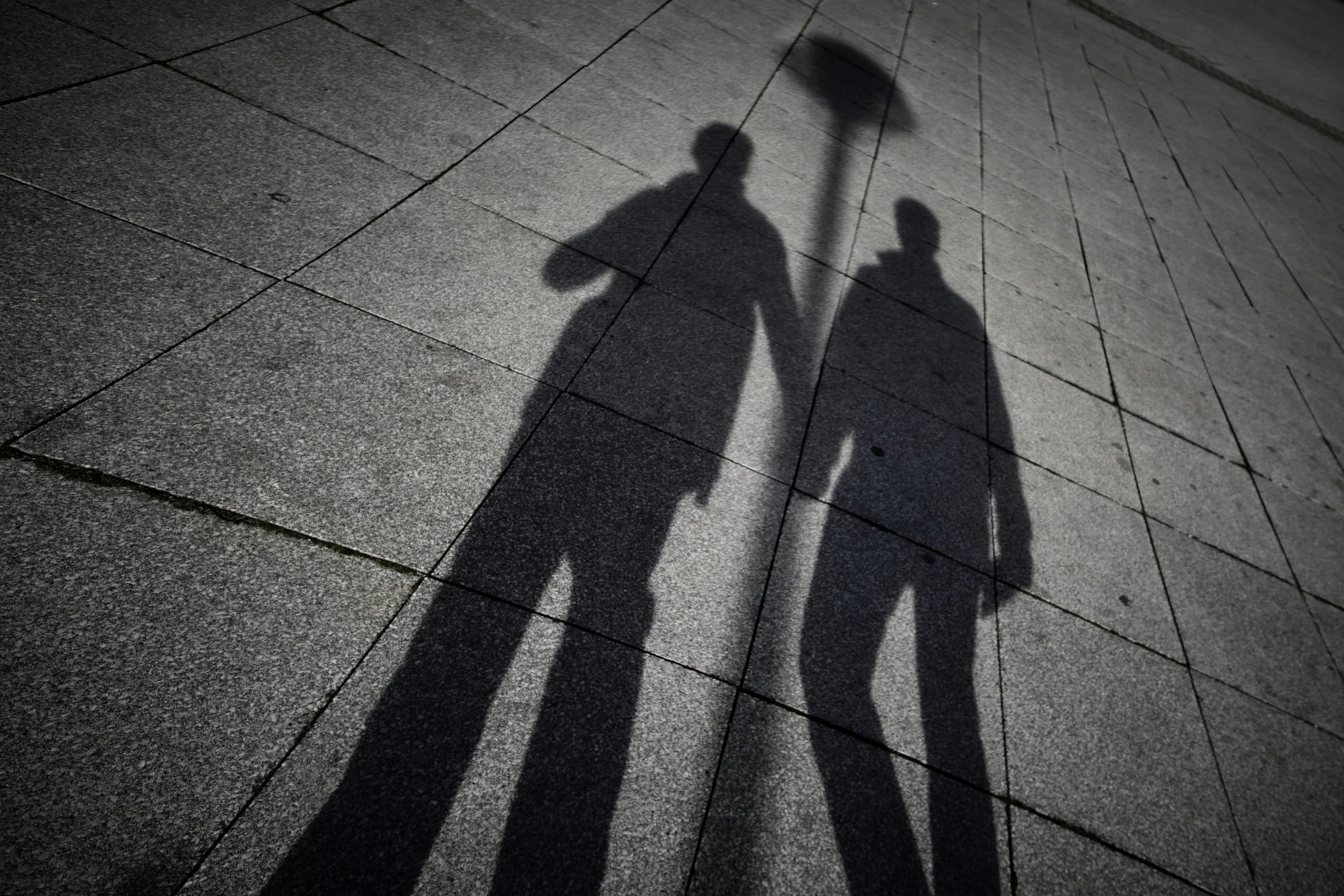 The shadows of two men holding hands on sidewalk.